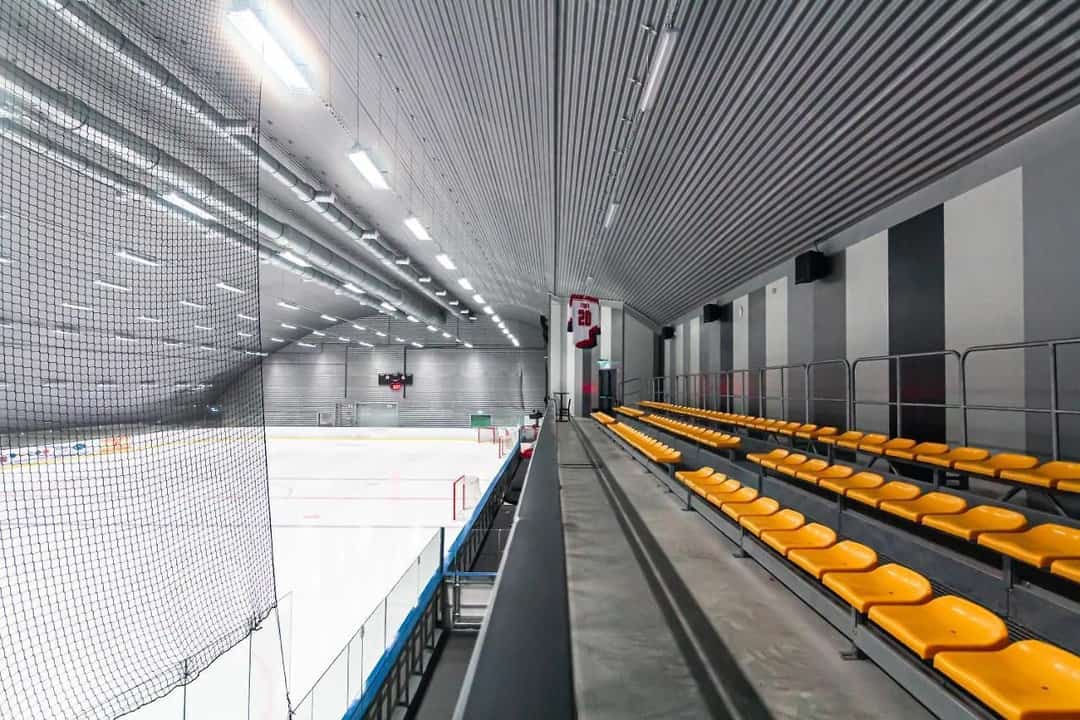 Montovaná ocelová oblouková hokejová hala Bruck – tribuny s plastovými sedadly a výhledem na ledovou plochu, moderní interiér s akustickým obkladem, realizace HUPRO SYSTEMS SE.