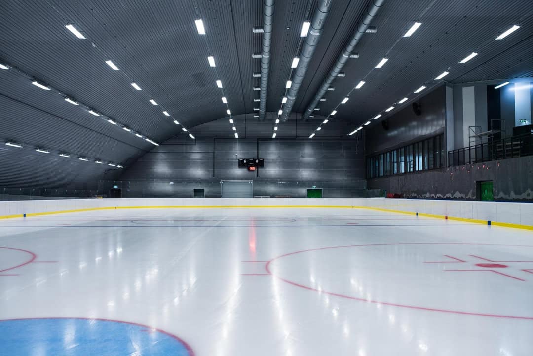 Montovaná ocelová oblouková hokejová hala Bruck – ledová plocha s tribunou a moderním osvětlením, architektonicky čistý interiér, realizace HUPRO SYSTEMS SE.