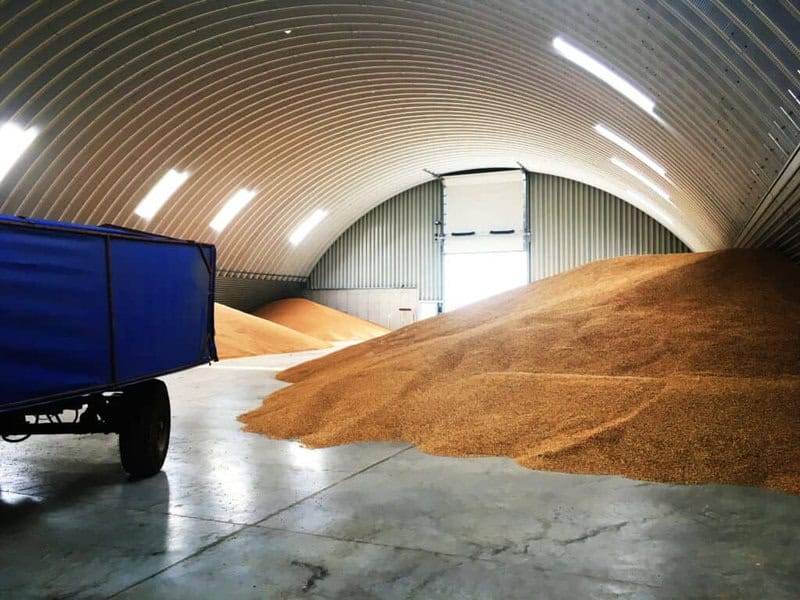 Montovaná ocelová oblouková zemědělská hala využívaná pro skladování obilí, s betonovou podlahou a velkými zásobami zrna uvnitř, realizace HUPRO SYSTEMS SE.
