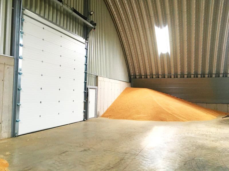 Montovaná ocelová oblouková zemědělská hala s betonovou podlahou, sekčními vraty a uskladněným obilím, interiér s trapézovým opláštěním, realizace HUPRO SYSTEMS SE.