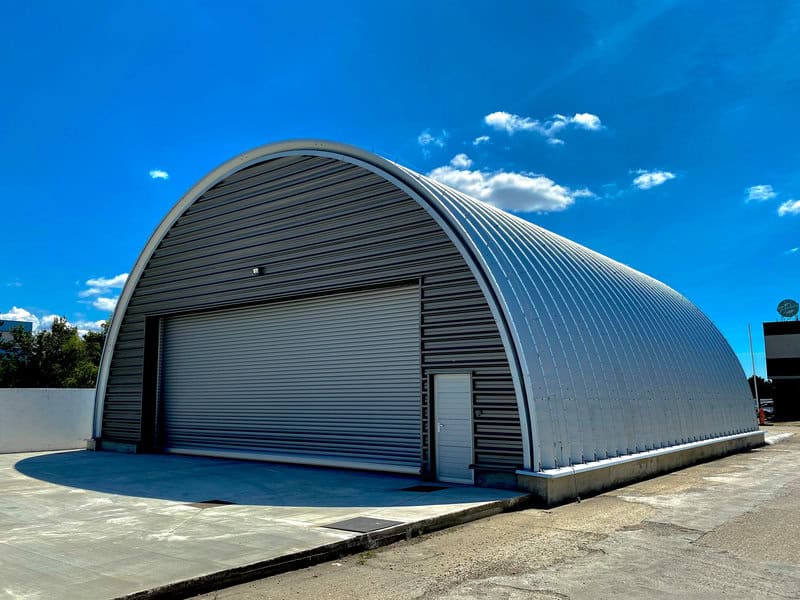 Moderní montovaná ocelová oblouková zemědělská hala se sekčními vraty a vedlejším vstupem, samonosná konstrukce bez vnitřních podpěr, realizace HUPRO SYSTEMS SE.