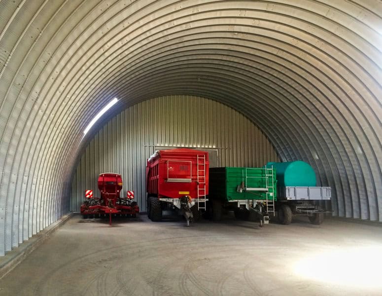 Interiér montované ocelové obloukové zemědělské haly s uskladněnou zemědělskou technikou, traktory a přívěsy, realizace HUPRO SYSTEMS SE.