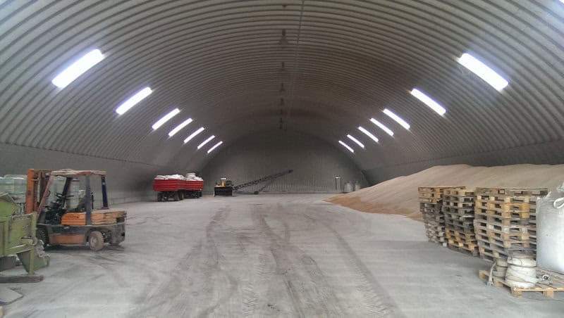 Interiér ocelové obloukové zemědělské haly s uskladněným obilím, paletami a zemědělskou technikou, realizace HUPRO SYSTEMS SE.