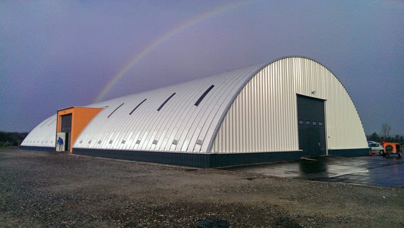 Moderní ocelová oblouková zemědělská hala s bočním vstupem a barevným portálem, nad halou je vidět duha. Realizace HUPRO SYSTEMS SE.