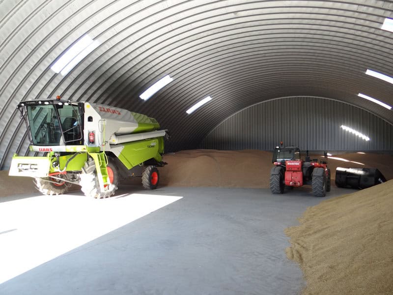 Interiér ocelové obloukové zemědělské haly s uskladněným obilím a zemědělskou technikou CLAAS a MANITOU. Realizace HUPRO SYSTEMS SE.