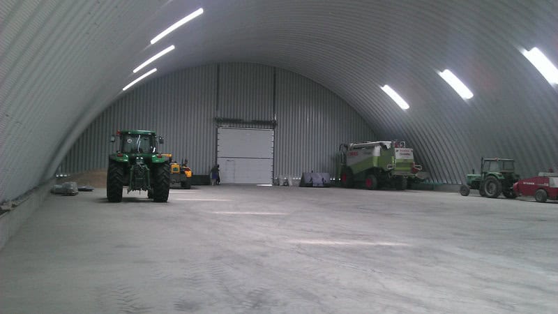 Interiér ocelové obloukové zemědělské haly s parkovanou zemědělskou technikou včetně traktorů a kombajnu CLAAS. Realizace HUPRO SYSTEMS SE.