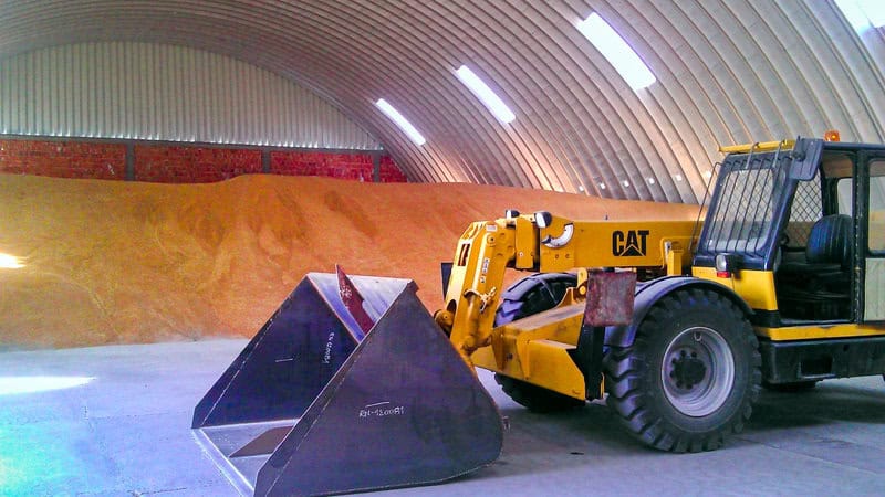 Interiér ocelové obloukové zemědělské haly s uskladněným obilím a pracovním strojem značky CAT. Realizace HUPRO SYSTEMS SE.