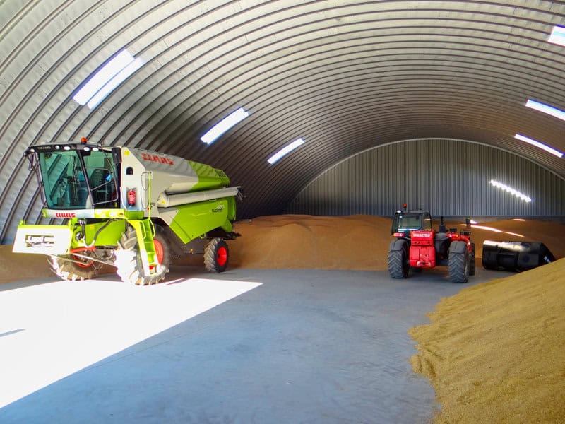 Interiér ocelové montované obloukové haly se sklizeným obilím, kombajnem a traktorem. Moderní skladové prostory pro zemědělskou produkci od HUPRO SYSTEMS SE.