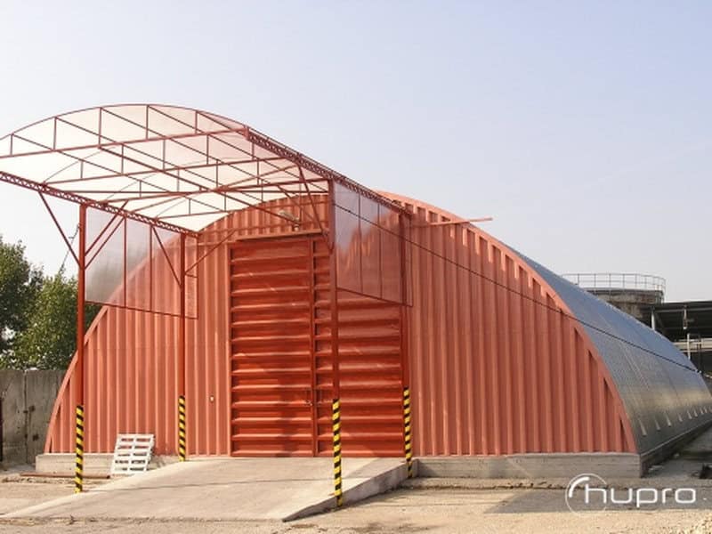 Moderní oblouková ocelová hala v červené barvě se vstupní stříškou z průsvitného materiálu. Realizace HUPRO SYSTEMS SE.