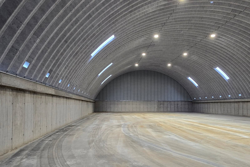 Moderní betonová oblouková zemědělská hala HUPRO SYSTEMS SE s vysokými stěnami a osvětlením, vhodná pro skladování obilí nebo zemědělské techniky.