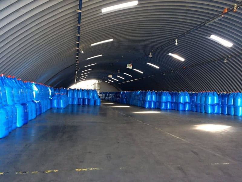 Oblouková ocelovová montovaná armádní hala s kovovou konstrukcí využívaná ke skladování materiálu v modrých barelech, realizace HUPRO SYSTEMS SE