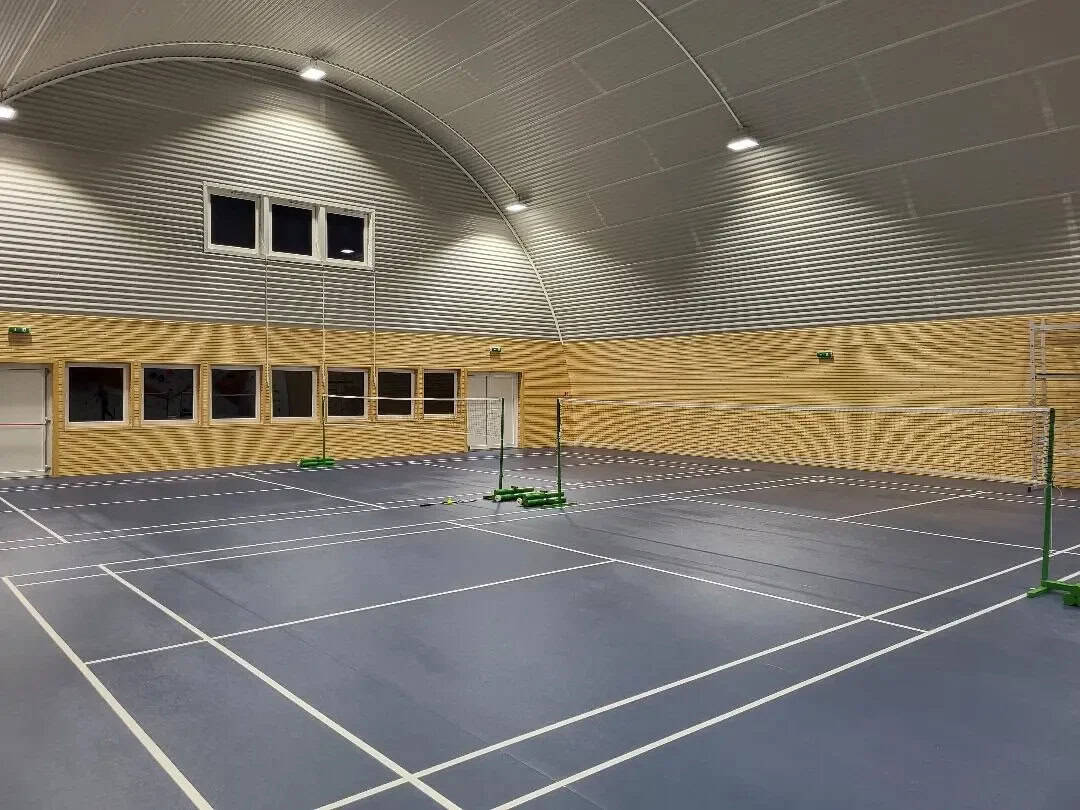 Interiér moderní obloukové sportovní haly HUPRO v Chorvátskom Grobe s badmintonovými kurty, dřevěným obkladem stěn a ocelovou konstrukcí systému HUPRO SYSTEMS SE.