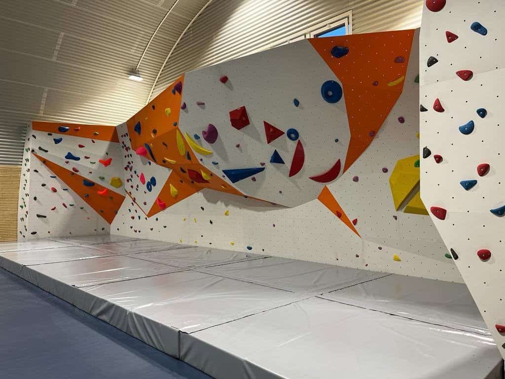 Lezecká stěna v moderní obloukové sportovní hale v Chorvátskom Grobe s barevnými úchyty a žíněnkami pro bezpečné lezení, hala postavená systémem HUPRO SYSTEMS SE.