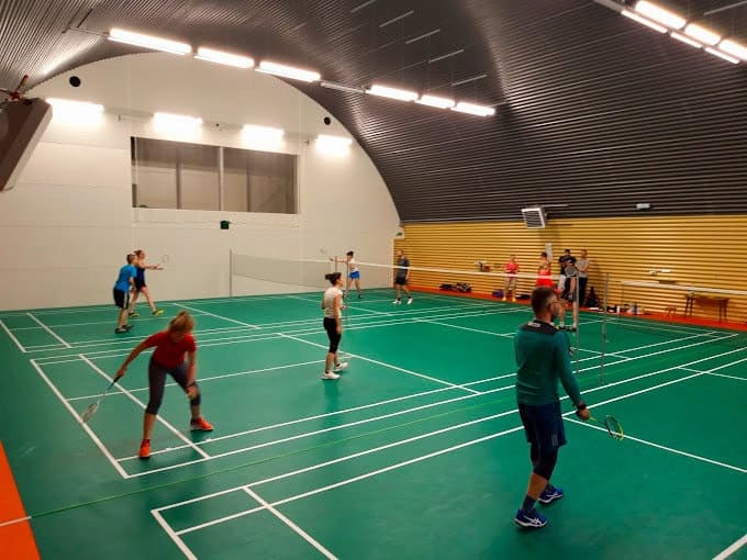 Interiér badmintonové montované ocelové obloukové haly v Paskově s několika kurty, hráči při hře a moderním osvětlením. Realizace HUPRO SYSTEMS SE.