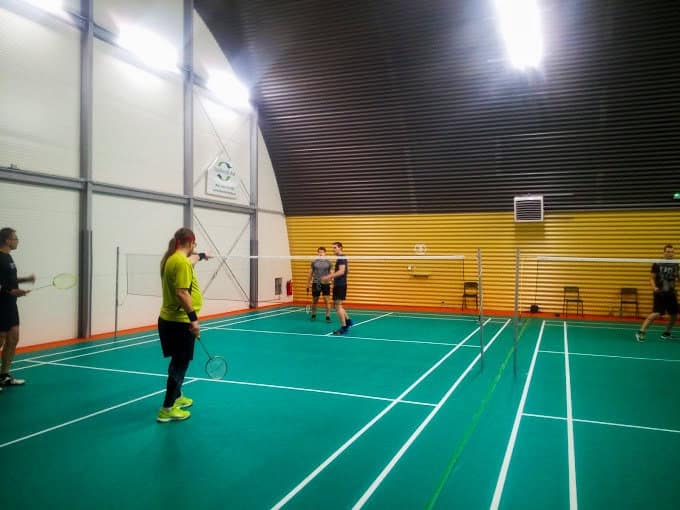 Skupina hráčů hraje badminton v moderní obloukové hale v Paskově s profesionálním zeleným povrchem a osvětlením. Realizace HUPRO SYSTEMS SE.