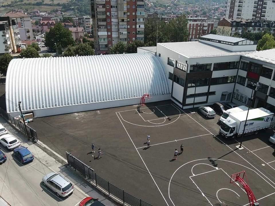 Montovaná ocelová plavecká hala Novi Pazar – letecký pohled na moderní krytý bazén navazující na školní komplex s venkovním sportovním hřištěm, realizace HUPRO SYSTEMS SE.
