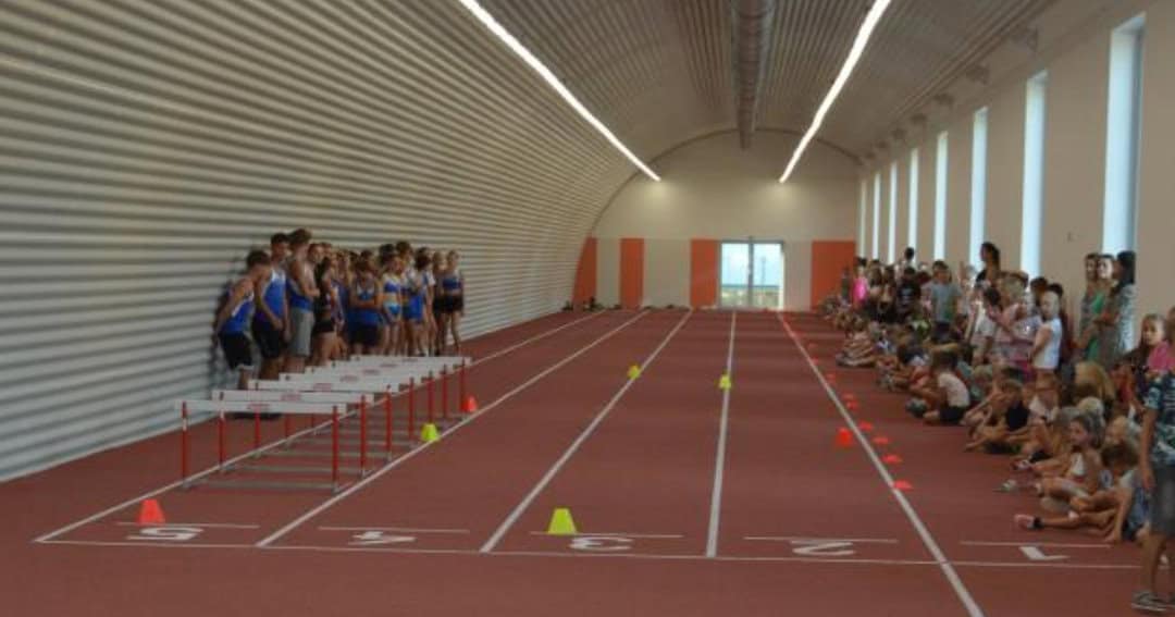 Sportovní hala v Prostějově s obloukovou ocelovou konstrukcí HUPRO SYSTEMS SE, určená pro atletiku, sprinty a tréninkové aktivity, s moderním zázemím a přilehlou venkovní plochou.