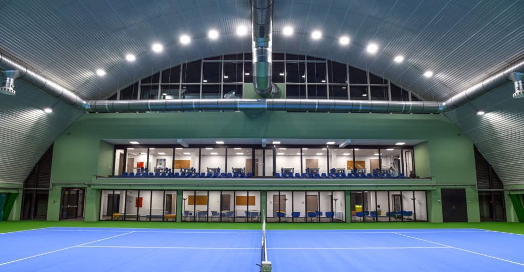 Montovaná ocelová tenisová hala Debrecín – interiér se čtyřmi kurty a zázemím pro diváky. Realizovala společnost HUPRO SYSTEMS SE.