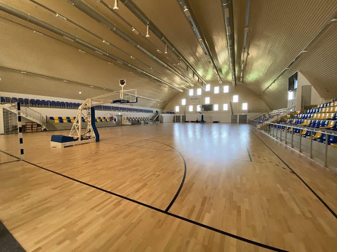 Interiér montované sportovní haly Fót Phoenix Sportcsarnok s basketbalovým hřištěm, dřevěnou podlahou a tribunami, realizace HUPRO SYSTEMS SE.