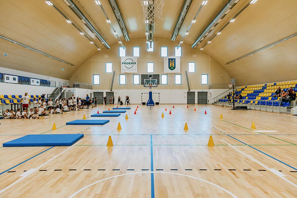 Sportovní hala Fót Phoenix Sportcsarnok s multifunkčním hřištěm, dřevěnou podlahou a tribunou, postavená společností HUPRO SYSTEMS SE.