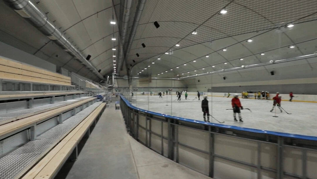 Montovaná ocelová hokejová hala Győr Nemak s ledovou plochou a trénujícími hokejisty, moderní sportovní objekt realizovaný společností HUPRO SYSTEMS SE.