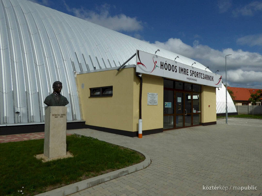 Oblouková sportovní hala Hajdúnánás s památníkem Hódose Imreho před vstupem, realizace HUPRO SYSTEMS SE.
