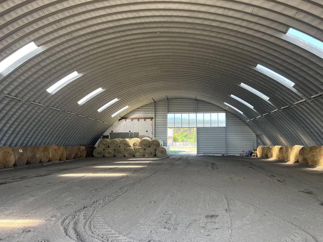 Interiér jízdárny v Břeclavi s obloukovou ocelovou konstrukcí a balíky sena uloženými podél stěn. Realizace HUPRO SYSTEMS SE.