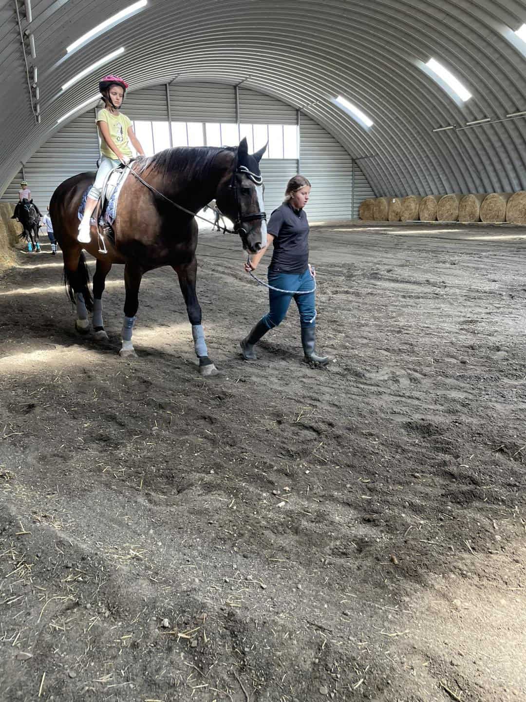 Dívka na koni při výcviku v jízdárně v Břeclavi s trenérkou, uvnitř obloukové ocelové montované haly. Realizace HUPRO SYSTEMS SE.