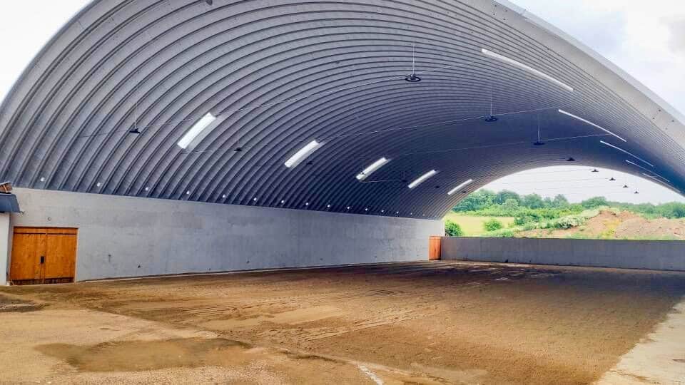 Interiér kryté jezdecké haly v Malé Bare s obloukovou ocelovou konstrukcí a pískovým povrchem pro trénink koní, postavené systémem HUPRO SYSTEMS SE.