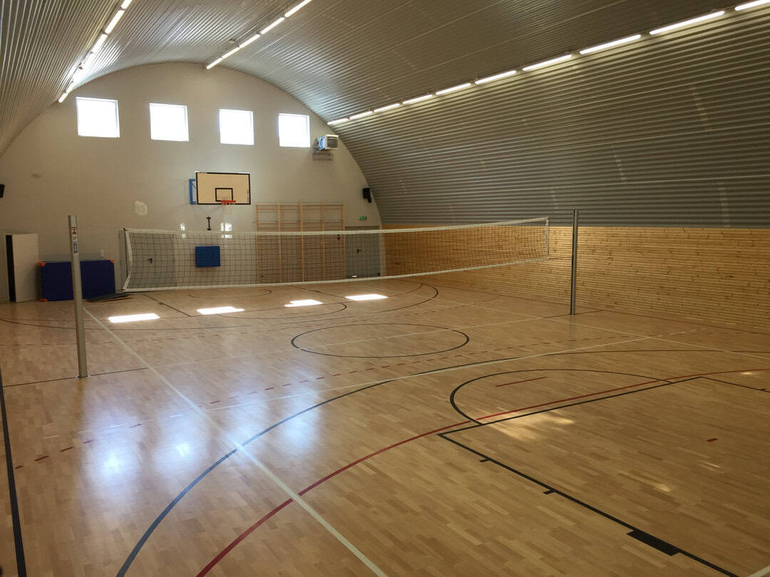 Montovaná ocelová oblouková sportovní hala Lodž, interiér s dřevěnou sportovní podlahou, basketbalovým košem a volejbalovým hřištěm. Realizovala společnost HUPRO SYSTEMS SE.