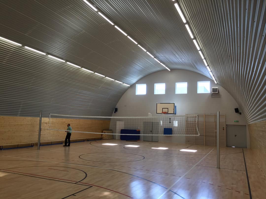Montovaná ocelová oblouková víceúčelová sportovní hala Lodž, interiér s dřevěnou podlahou, basketbalovým košem a volejbalovým hřištěm. Realizace společnosti HUPRO SYSTEMS SE.