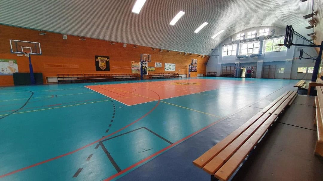 Montovaná ocelová oblouková víceúčelová sportovní hala Milicz, interiér s basketbalovým a volejbalovým hřištěm, moderní dřevěné obložení. Realizovala společnost HUPRO SYSTEMS SE.
