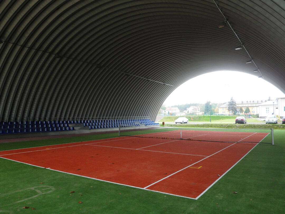 Montovaná ocelová oblouková tenisová hala Tomaszów Lubelski, interiér s tenisovým kurtem a tribunou. Realizovala společnost HUPRO SYSTEMS SE.