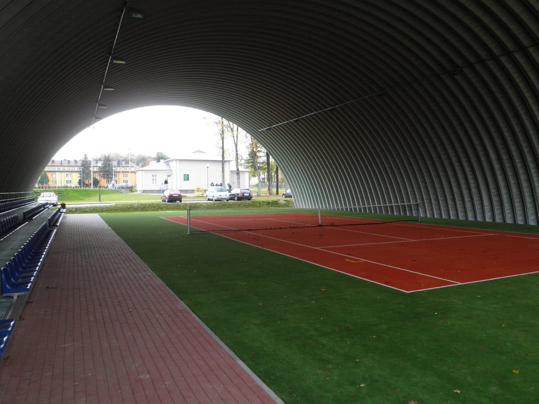 Montovaná ocelová oblouková tenisová hala Tomaszów Lubelski, interiér s tenisovým kurtem a pohled od tribuny. Realizovala společnost HUPRO SYSTEMS SE.