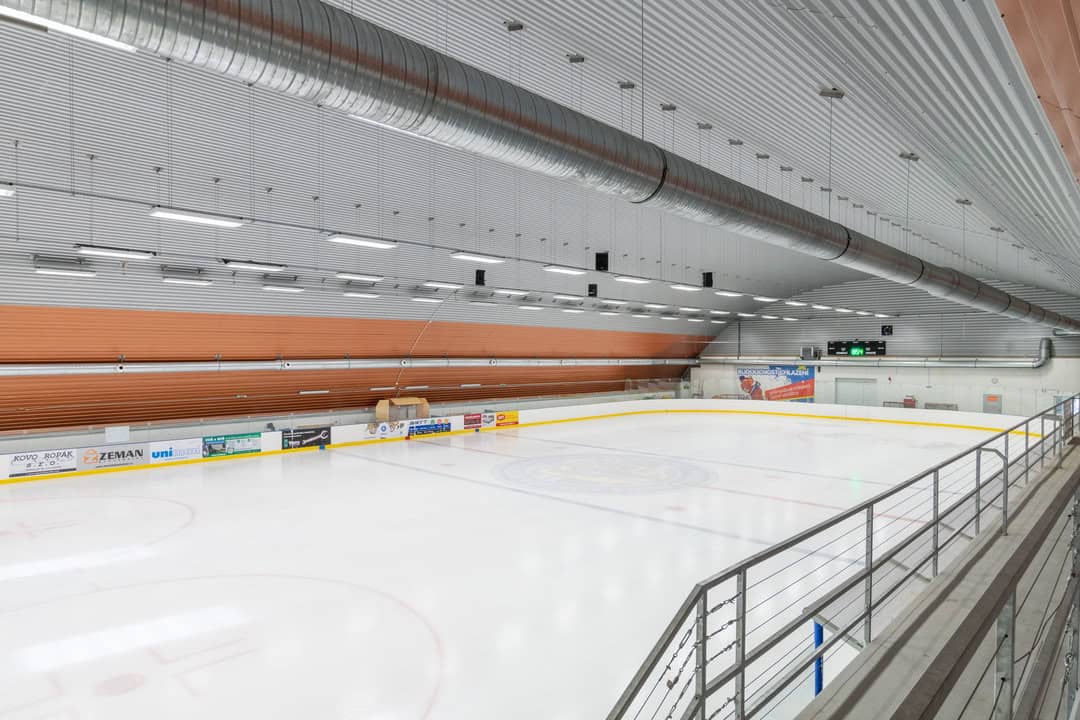 Interiér zimního stadionu v Bystřici nad Pernštejnem s ledovou plochou, tribunou a ocelovou obloukovou konstrukcí. Realizace HUPRO SYSTEMS SE.