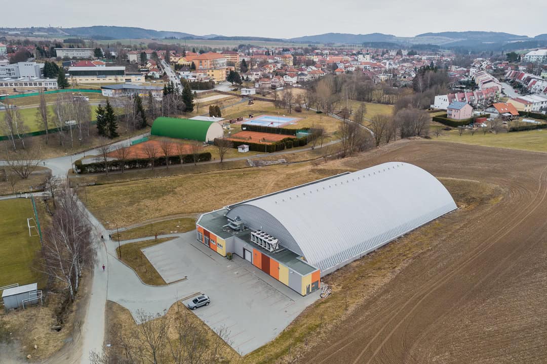 Letecký pohled na zimní stadion v Bystřici nad Pernštejnem s obloukovou střechou a okolním sportovním areálem, realizace HUPRO SYSTEMS SE.