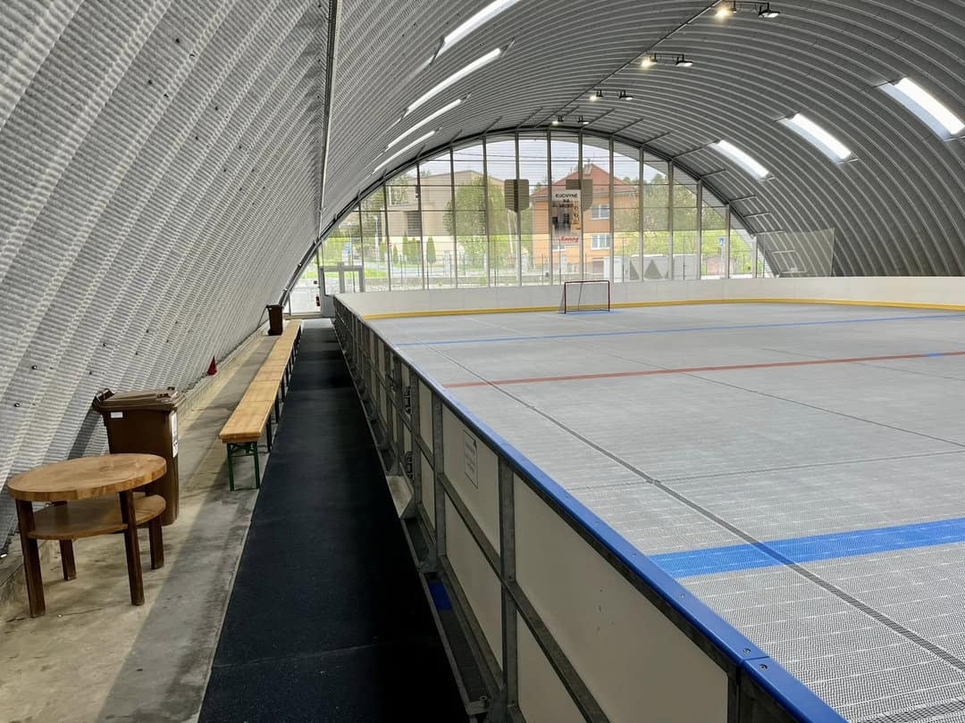 Boční pohled do multifunkční sportovní haly v Lipanech s plastovým povrchem pro hokejbal, lavicemi pro hráče a moderní obloukovou ocelovou konstrukcí od HUPRO SYSTEMS SE.