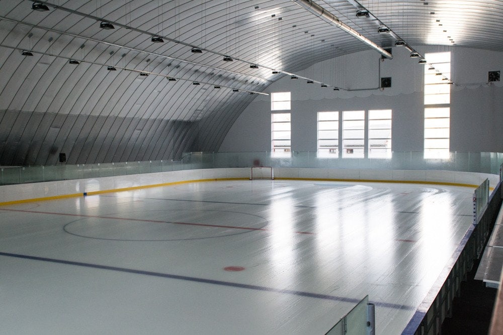 Interiér hokejové haly HUPRO Aréna v Nitře – Klokočině s prázdnou ledovou plochou, montovaná ocelová konstrukce s moderním osvětlením a prosklenými mantinely.