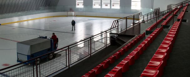 Interiér hokejové haly HUPRO Aréna v Nitře – Klokočině s červenými tribunami, ledovou plochou a rolbou připravující led, montovaná ocelová konstrukce od HUPRO SYSTEMS SE.