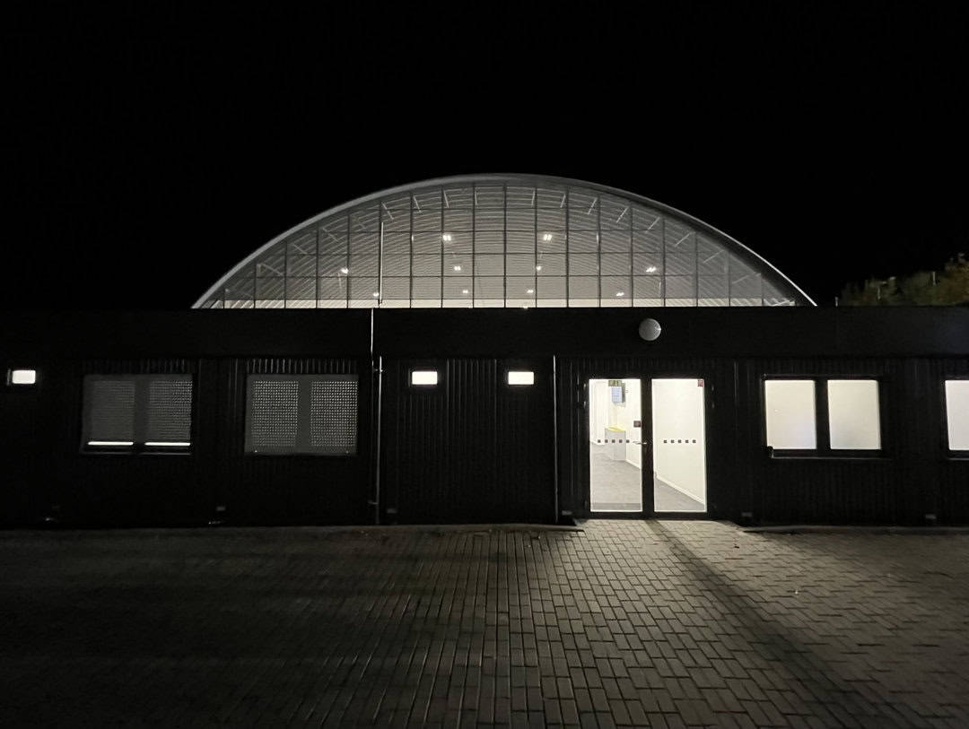 SPM Arena Praha – noční pohled na vstupní část hokejové haly s prosvětlenou obloukovou konstrukcí. Realizace HUPRO SYSTEMS SE.