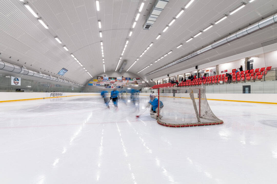 Zimní stadion Telč – ledová plocha s probíhajícím hokejovým tréninkem, červené tribuny pro diváky a moderní oblouková montovaná ocelová hala od firmy HUPRO SYSTEMS SE.