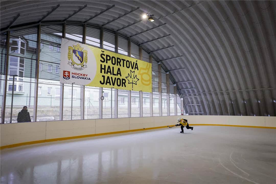 Interiér sportovní haly Javor v Tvrdošíně s ledovou plochou a hokejistou v akci, moderní ocelová hala postavená systémem HUPRO SYSTEMS SE.