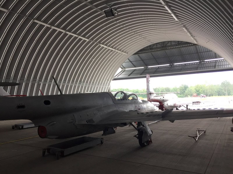 Oblouková ocelová montovaná letecká hala s vojenskými letouny, vhodná pro parkování a servis letadel. Odolná konstrukce zaručuje dlouhou životnost a bezpečné zázemí. Realizace HUPRO SYSTEMS SE.