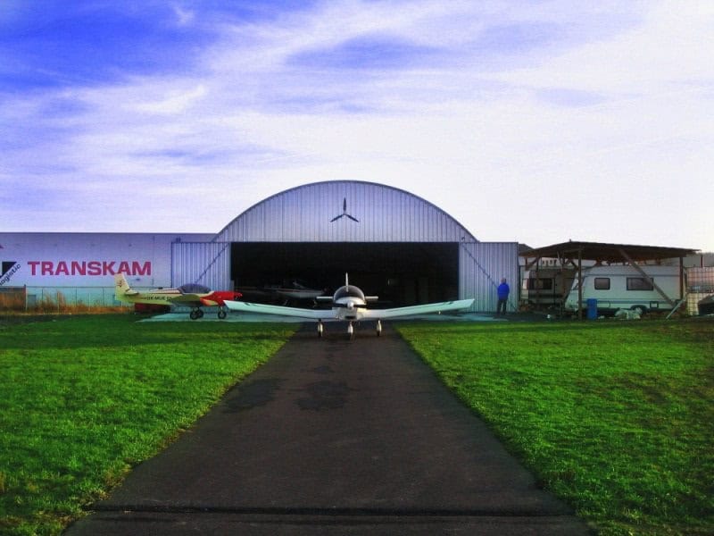 Oblouková ocelová montovaná letecká hala s malými sportovními letadly před hangárem, samonosná konstrukce HUPRO SYSTEMS SE