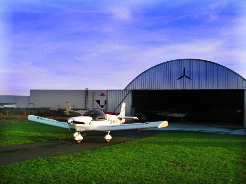 Oblouková ocelová montovaná letecká hala s lehkým sportovním letadlem před hangárem, samonosná konstrukce HUPRO SYSTEMS SE