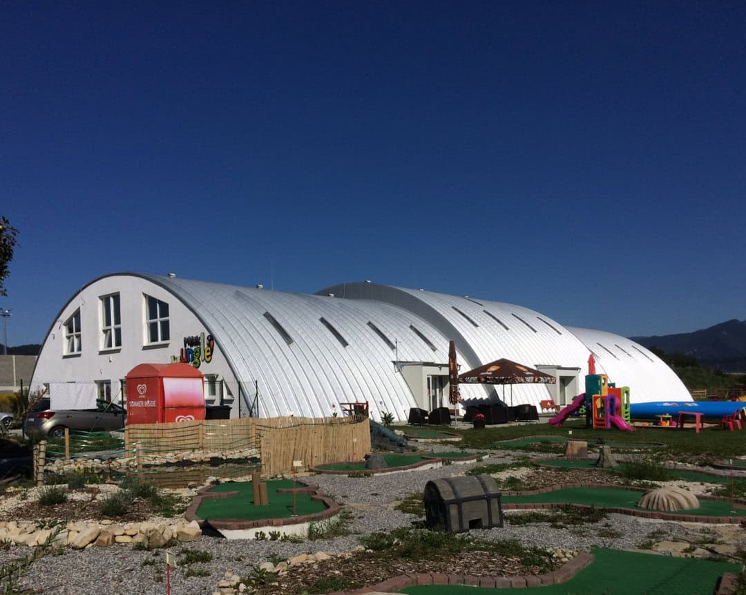 Oblouková ocelová montovaná hala využitá jako moderní víceúčelová budova s dětským hřištěm a kavárnou. Realizace HUPRO SYSTEMS SE.