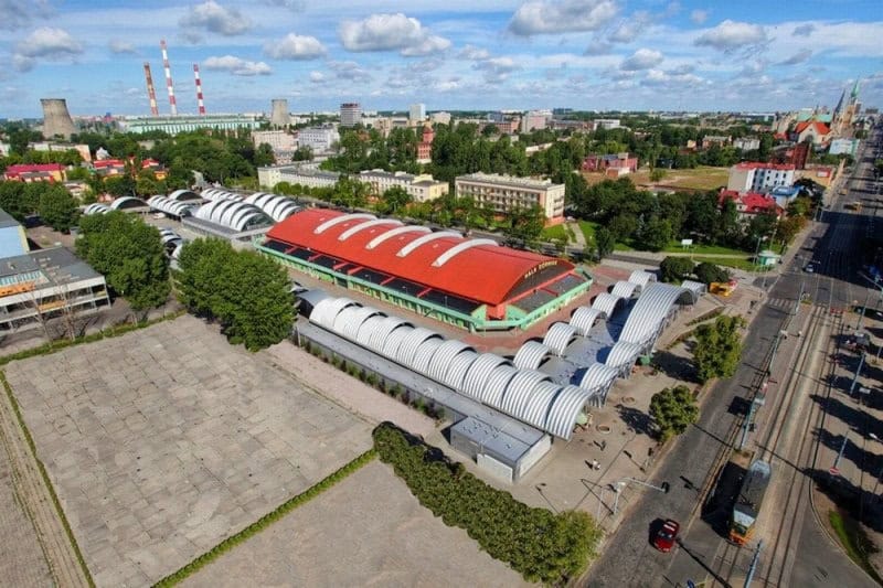 Letecký pohled na moderní obloukové ocelové haly HUPRO® s červenou střechou a obchodními prostory. Ocelové haly HUPRO SYSTEMS SE.