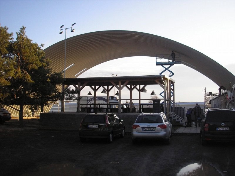 Oblouková ocelová hala s dřevěným přístřeškem a venkovním posezením, konstrukce ve fázi montáže, realizace HUPRO SYSTEMS SE.