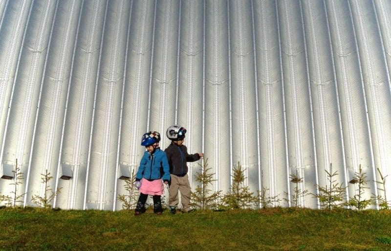 Detail obloukové ocelové haly s vlnitým plechem, děti stojící u fasády konstrukce, realizace HUPRO SYSTEMS SE.