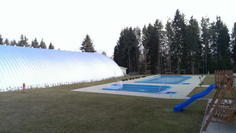 Oblouková ocelová hala na míru umístěná u venkovního bazénu a dětského hřiště, realizace HUPRO SYSTEMS SE.